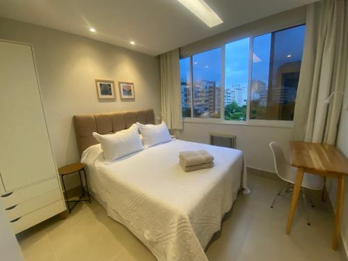 um quarto com uma cama com lençóis brancos e uma janela em Três suítes há poucos passos da praia no Rio de Janeiro