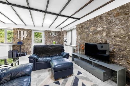 a living room with leather furniture and a stone wall at Beautiful renovated former coach house in Llandeilo