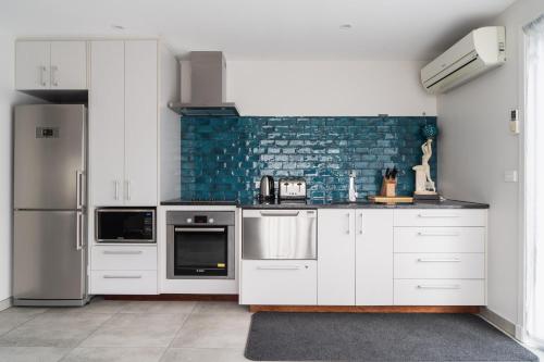 a kitchen with white cabinets and a blue brick wall at Lavender Box in Dunedin