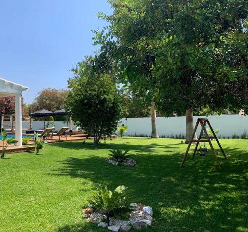 a yard with a tree and a swing set at Bungalow Madeira - Casa das Lages - Almancil - Quinta do Lago in Almancil