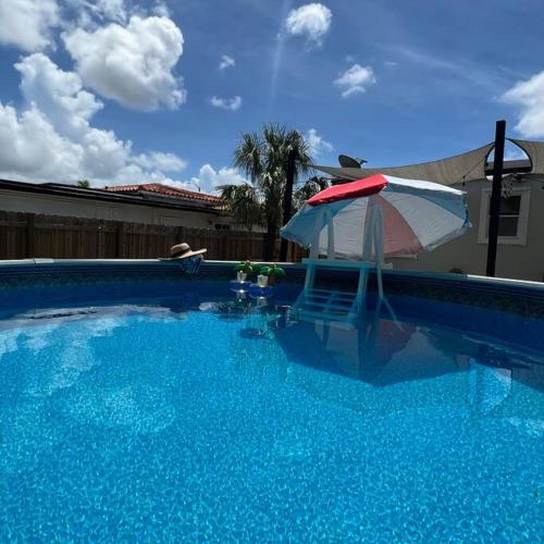 a large blue swimming pool with an umbrella and a chair at Coral Gables Home with POOL Near Airport. King beds in Miami