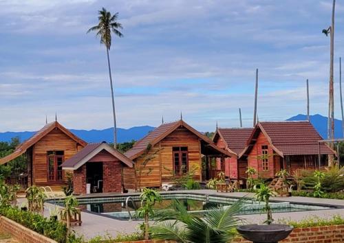a group of wooden buildings with a palm tree in the background at PULANG RESORT in Setiu