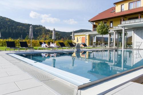 a swimming pool with people sitting on chairs next to a house at Mosers Blume Relax & Genuss Hotel in Haslach im Kinzigtal