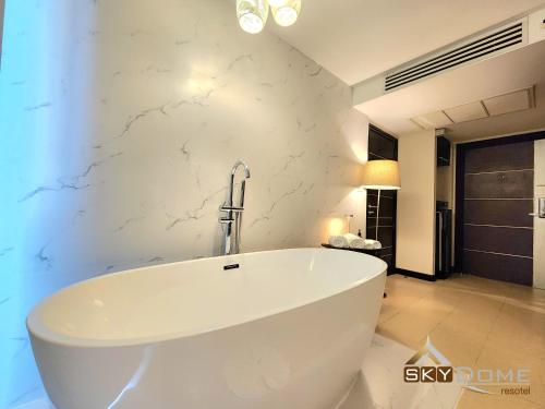 a bath tub in a bathroom with a white wall at Sky dome resotel - โรงแรมสกายโดม รีโซเทล in Bangkok