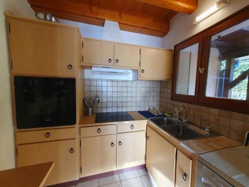cocina con armarios de madera, fregadero y ventana en Le Chant du Loriot en Labaroche