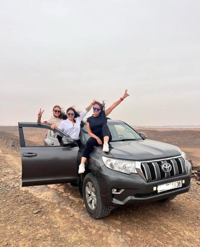 three people sitting in the back of a car in the desert at Desert Berber Fire Camp in Merzouga