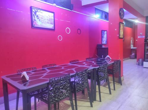 Habitación con pared roja, mesa y sillas. en Hotel 7 Eleven en Dirāng