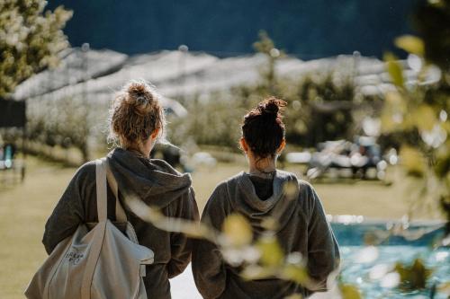 two women walking down a path near a swimming pool at Apfelhotel Torgglerhof in Saltusio