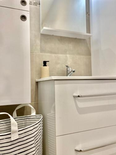 - une cuisine blanche avec un évier et un panier dans l'établissement Maison Mer & Jardin Ouistreham Riva-Bella, à Ouistreham