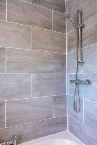 a shower in a bathroom with a tile wall at Cosy Northumbrian Cottage in Barrasford