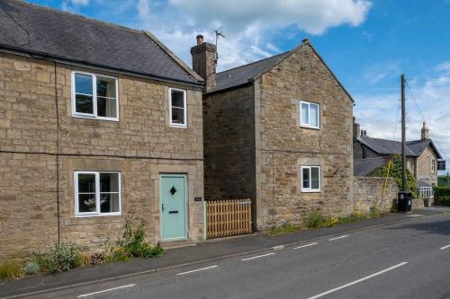 una casa de ladrillo con una puerta azul en una calle en Cosy Northumbrian Cottage, en Barrasford