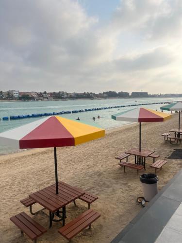 a group of picnic tables and umbrellas on a beach at درة العروس غرفة وصالة مع بلكونة مطلة على شاطئ البردايس-عوائل in Durat  Alarous