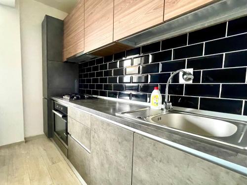 uma cozinha com um lavatório e uma parede de azulejos pretos em YamaLux Apartments - Cozy Double - WestSide 3 em Floresti