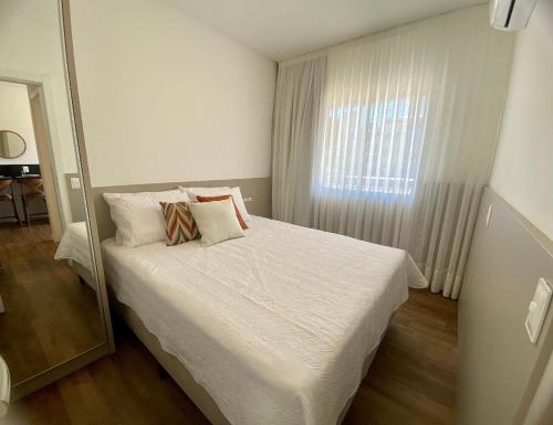 a bedroom with a bed with white sheets and a window at Vila do Centro Bombinhas in Bombinhas
