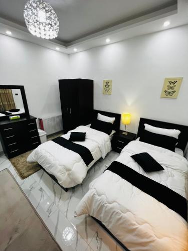1 dormitorio con 2 camas y lámpara de araña en شقة مفروشة بغرفتي نوم الجاردنز en Umm Uthainah