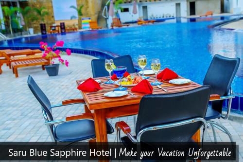 uma mesa de madeira com cadeiras e copos de vinho ao lado de uma piscina em Saru Blue Sapphire Hotel em Godakewela