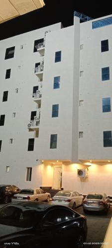 ein großes weißes Gebäude mit Autos auf einem Parkplatz in der Unterkunft أجنحة فندقية مفروشة عوائل فقط in Bisha