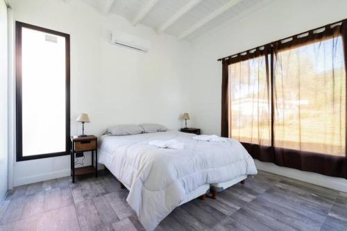 a white bedroom with a bed and a large window at Perseo 1422 in Pinamar