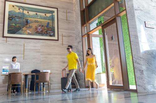 a man and woman walking through a building with a suitcase at Cat Ba Paradise Hotel - Sky Bar & Massage in Cat Ba