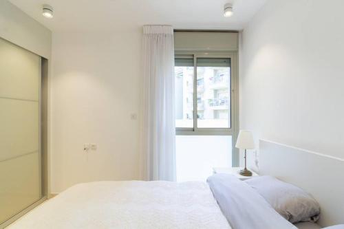 a white bedroom with a bed and a window at Jaffa's Hideaway - Lux 2BR w/balcony and parking! in Tel Aviv