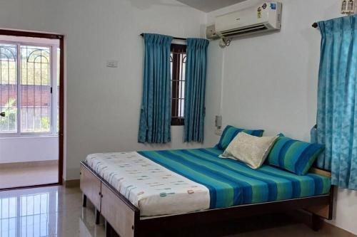 a bedroom with a bed with blue curtains and a window at SHI's Alayam 3BHk Villa in Avinashi road, near Railway station in Pīlamedu