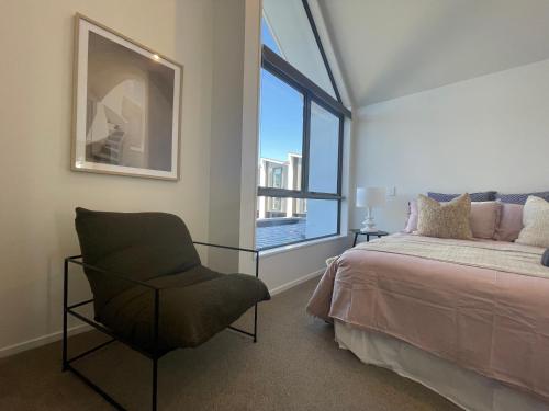 a bedroom with a bed and a chair and a window at Inner City Luxury With Free Parking in Christchurch