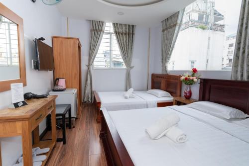 a room with two beds and a desk and two windows at Sunny Guesthouse in Ho Chi Minh City