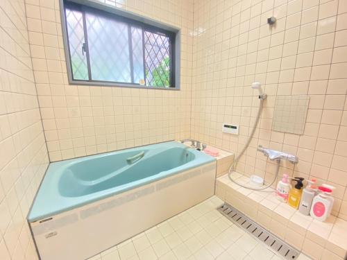 La salle de bains est pourvue d'une baignoire bleue et d'une fenêtre. dans l'établissement 島の宿　結んちゅ, à Amami