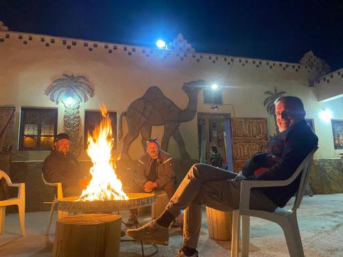 three men sitting around a fire in front of a building at Auberge & Restaurant Agoudal in Agoudal