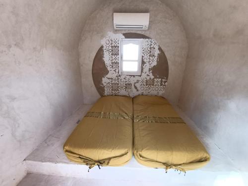 a bed in a small room with a window at L'Oasis in Ksar Ghilane