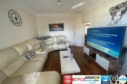 a living room with a large couch and a flat screen tv at Wollongong station holiday house with Wi-Fi,75 Inch TV, Netflix,Parking,Beach in Wollongong