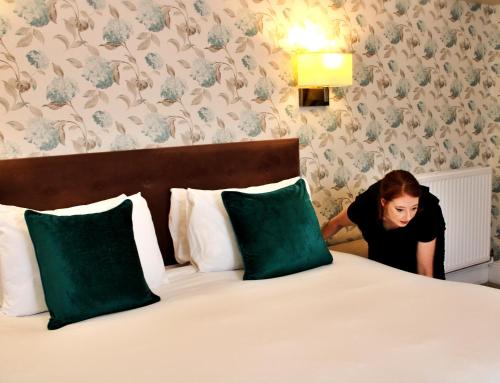 a woman is standing next to a bed at Victoria Square Hotel Clifton Village in Bristol