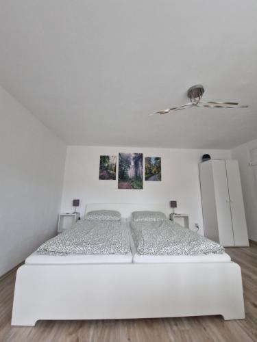 a white bed in a white bedroom with pictures on the wall at Waldbergperle Ernsbach in Forchtenberg