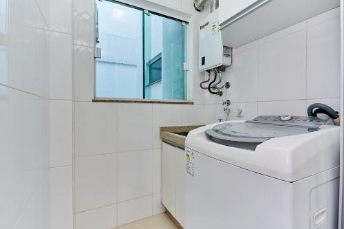 ein weißes Bad mit einer Waschmaschine und einem Fenster in der Unterkunft 1054 - Apartamento Centro de Bombinhas - Vista Mar - 1 Vaga Garagem - 50 metros Praia in Bombinhas