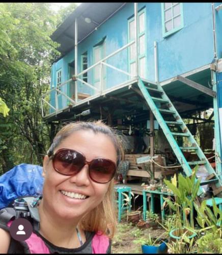 Eco Jungle Lodge Juara Tioman في جزيرة تيومان: امرأة ترتدي نظارة شمسية تقف أمام البيت الأزرق