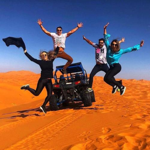 a group of people jumping in the desert at Sunset Camp Merzouga in Merzouga