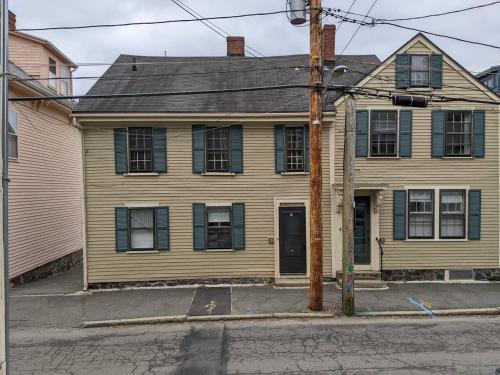 a yellow house with green shutters on a street at The Seabird Suite in Marblehead