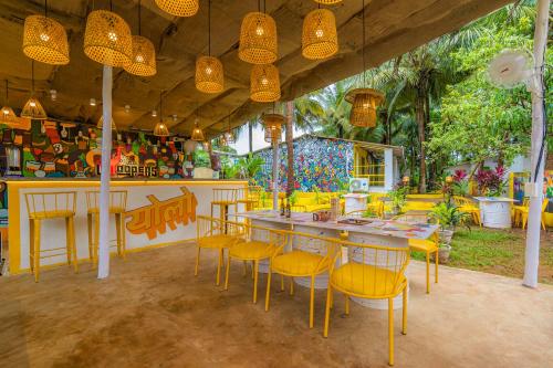 a restaurant with a bar with yellow chairs and tables at Whoopers Party Hostel, Palolem in Palolem