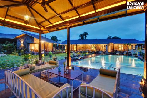 - une piscine avec des tables et des chaises en face d'un bâtiment dans l'établissement StayVista at The Earthen Boutique with Spacious Pool, Terrace, Lawn & Games, à Udaipur