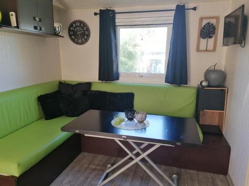a living room with a green couch and a table at Mobil-Home Cosy Climatisé 3 chambres in Vic-la-Gardiole