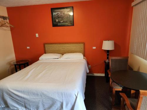 a bedroom with an orange wall with a bed and a table at Sunparlor Motel in Leamington