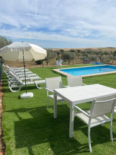 una mesa y sillas blancas con sombrilla y piscina en FINCA VALDELAJARA a 20 minutos de Puy du Fou en Toledo