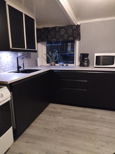 a kitchen with black cabinets and a sink and a microwave at Sommerstue Hessdalen in Ålen