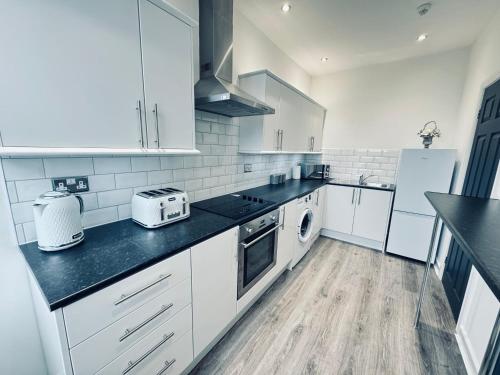 uma cozinha com armários brancos e bancadas pretas em Spanish City View, Stylish Sea Front Apartment Free Onsite Parking em Whitley Bay