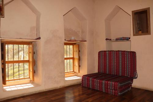a room with a chair and two windows at Misfah Old House in Misfāh