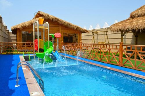 a pool with a water slide in front of a house at شاليهات الأكواخ الثلاثة in Khalij Salman