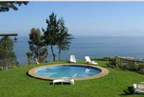 a swimming pool with two lawn chairs in the grass at Bahia Pelícanos Horcón depto. en primera línea in Puchuncaví