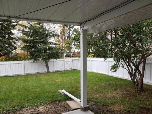 a white pergola in a yard with a tree at Sweethome - 10 min to Rogers Place & so much more in Edmonton