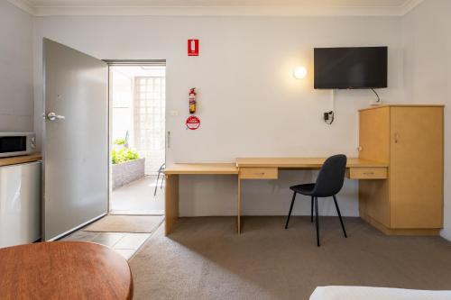a desk with a chair and a television on a wall at Port Aloha Motel in Port Macquarie