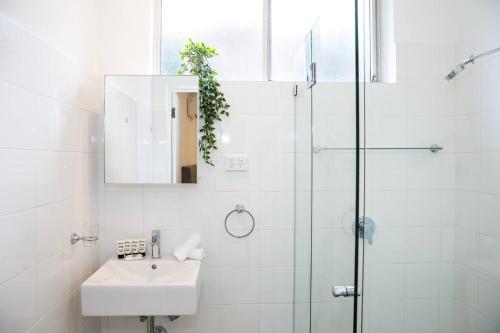 a white bathroom with a sink and a shower at Esperanza Gardens - A Stylish Victorian Studio in Sydney